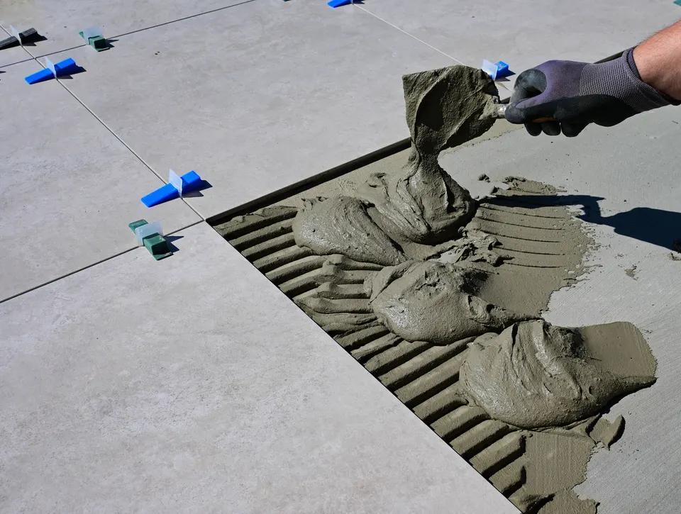 Gloved hand applying tile adhesive to a floor