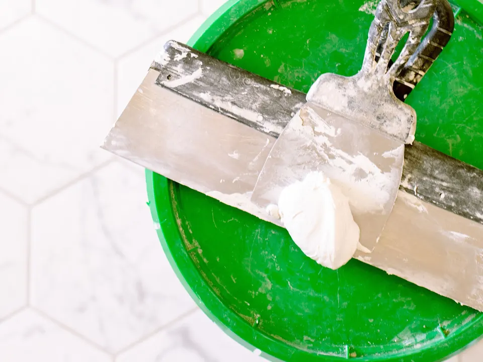 Putty knives and white wall putty on a green bucket lid