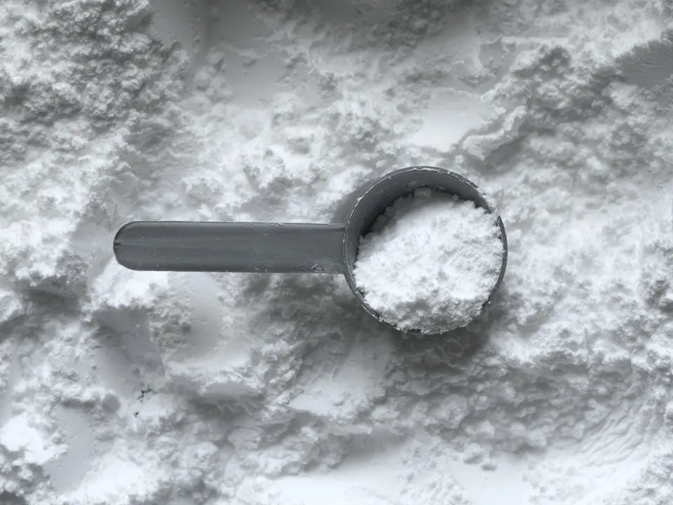 Grey scoop of fine white powder resting on a pile of powder
