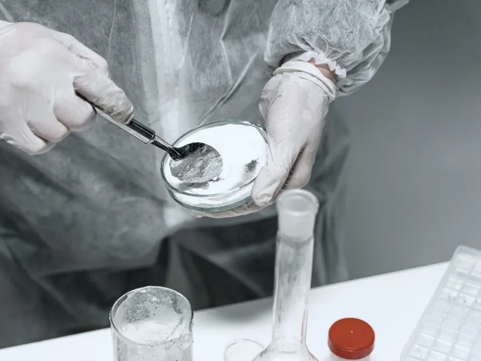 Fine white powder in a laboratory dish, held by a technician