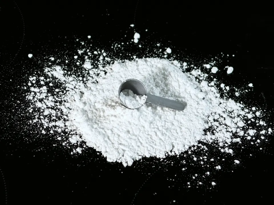 Fine white powder heaped on a dark surface with a small scoop